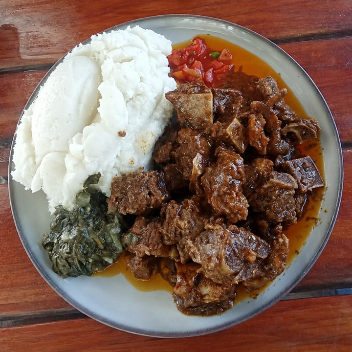 A plate of food on a wooden table, featuring a serving of white mashed potatoes, a green side dish, and a brown meat stew in a sauce.