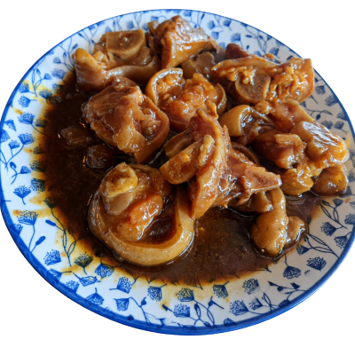 A close-up shot of  trotters - tlhakhwana pieces in a rich, dark brown sauce, served on a blue and white patterned ceramic plate against a white background.